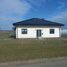 Nowoczesny dom jednorodzinny w Łazach z ciemną dachówką i panelami słonecznymi na dachu, widziany z poziomu ulicy.