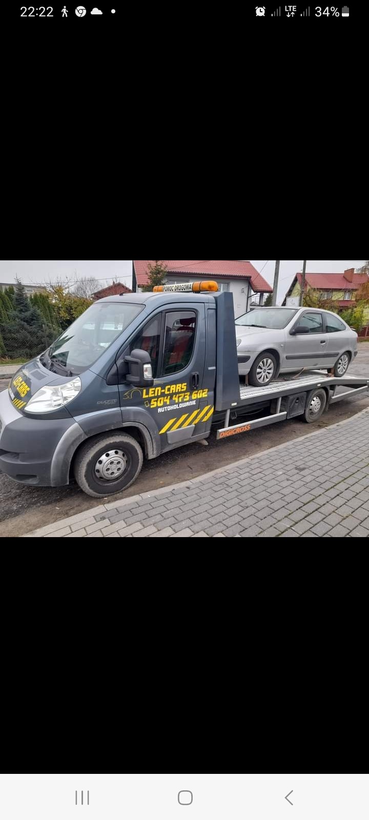 Szara laweta z zaparkowanym srebrnym samochodem osobowym na platformie, widoczny numer telefonu firmy i napis 'Pomoc Drogowa'.