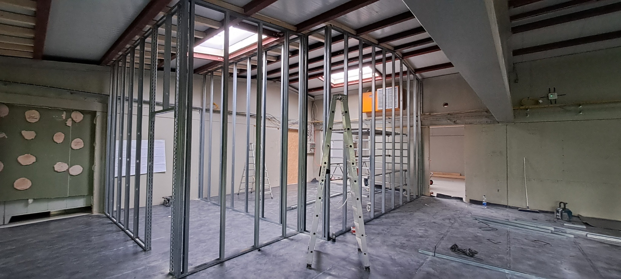 Wnętrze w trakcie budowy ścian działowych z metalowych profili, widoczna drabina, surowy stan wykończenia, oświetlenie górne, podłoga zabezpieczona folią.
