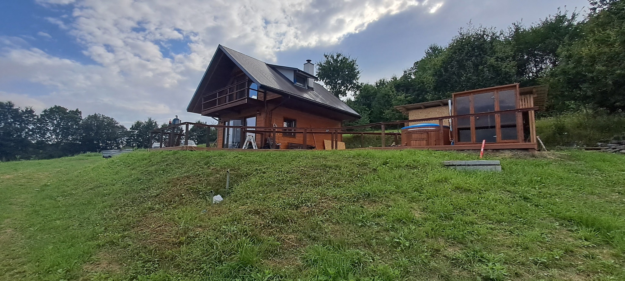 Drewniany dom z balkonem i jacuzzi na zewnątrz, widok z dołu na tle zachmurzonego nieba.