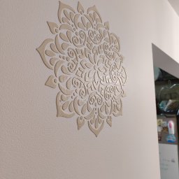 BurbanBud - Beżowy, wypukły wzór mandali na kremowej ścianie, z widoczną fakturą farby i fragmentem białej futryny drzwiowej w tle.