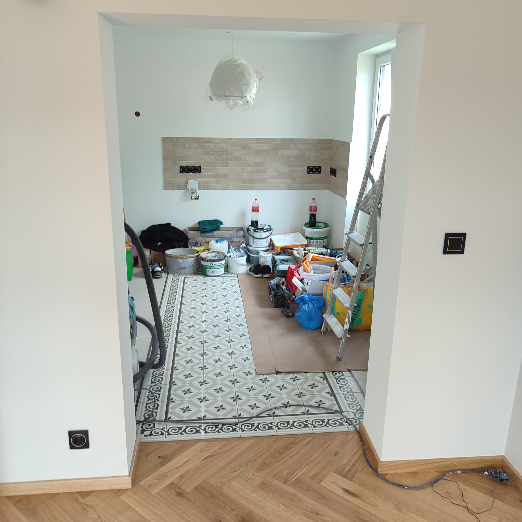 Remont kuchni w trakcie: ułożone płytki podłogowe z wzorem, ściany przygotowane pod malowanie, widoczne narzędzia i materiały budowlane, drabina oparta o ścianę.