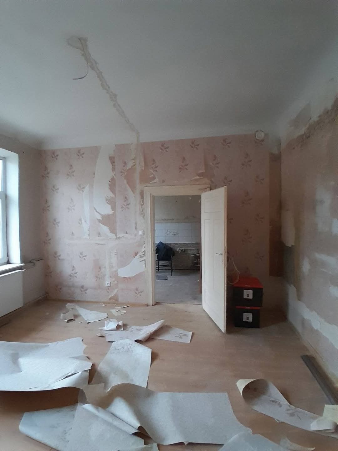 Pokój w trakcie usuwania starej tapety, widoczne fragmenty oderwanej tapety na podłodze i ścianach. Przygotowanie do malowania ścian.