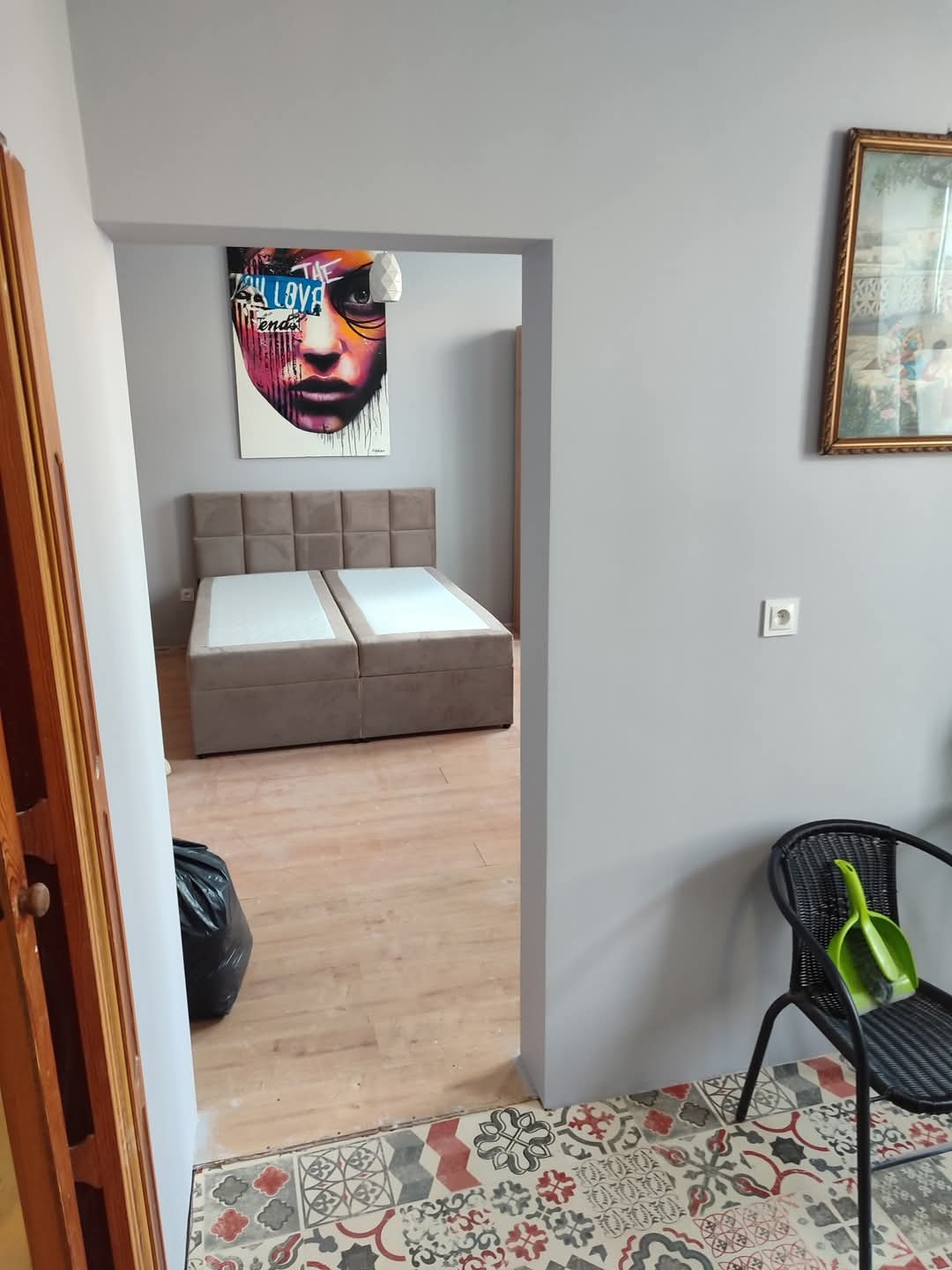 Szare wnętrze w trakcie wykańczania: widok na pokój z łóżkiem, malowane ściany, nowe płytki podłogowe w przedpokoju, krzesło z szufelką, worek na śmieci.