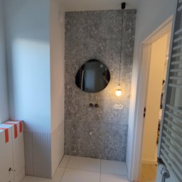 Maestro - Wykończona łazienka w Poznaniu: ściana z szarym wzorem, asymetryczne lustro, minimalistyczna lampa wisząca i białe płytki podłogowe. Nowoczesny design.