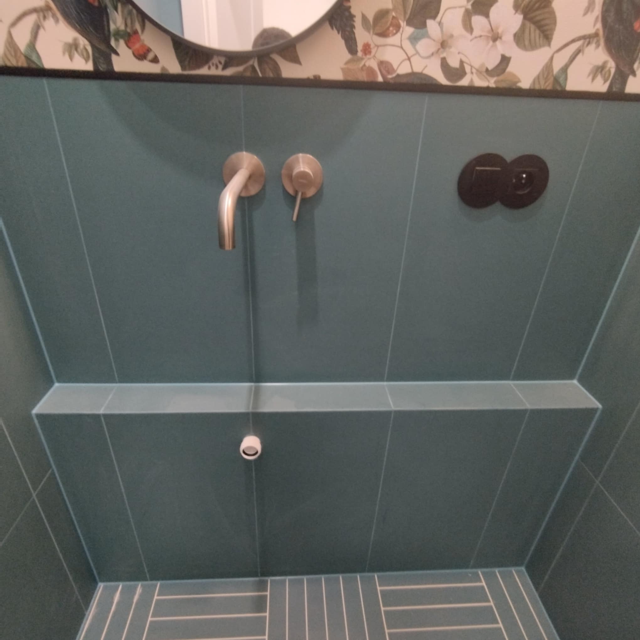 Wykończona łazienka z turkusowymi płytkami, baterią umywalkową w kolorze szczotkowanego złota i ozdobną tapetą z motywami roślinnymi nad umywalką.