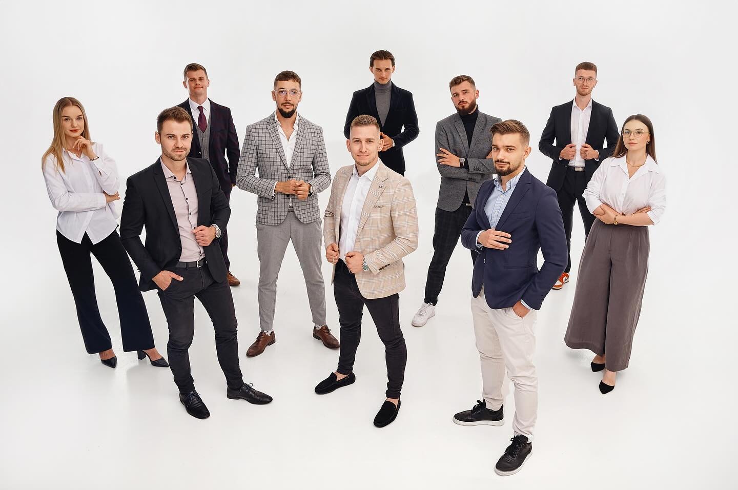 Zespół dziesięciu osób, kobiety i mężczyźni, ubrani w eleganckie, choć nieformalne stroje biznesowe, pozujący na białym tle, sugerujący profesjonalizm i nowoczesne podejście do biznesu.