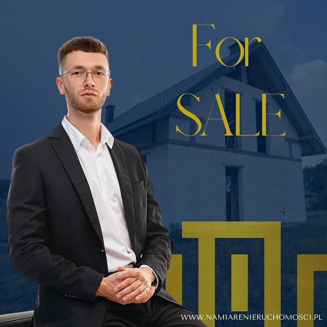 Młody mężczyzna w garniturze i okularach, na tle domu w stanie surowym i napisu 'For SALE', z widocznym tatuażem na dłoni.