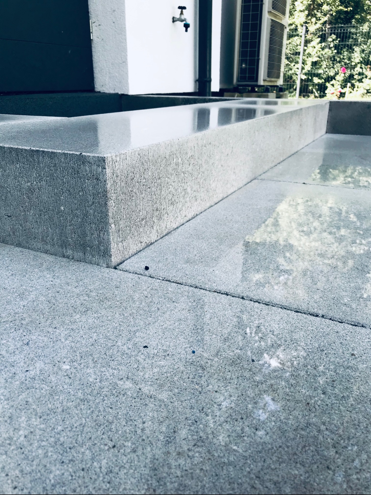 Szare, kamienne stopnie wejściowe do budynku, z widoczną teksturą kamienia i odbiciami na mokrej powierzchni.