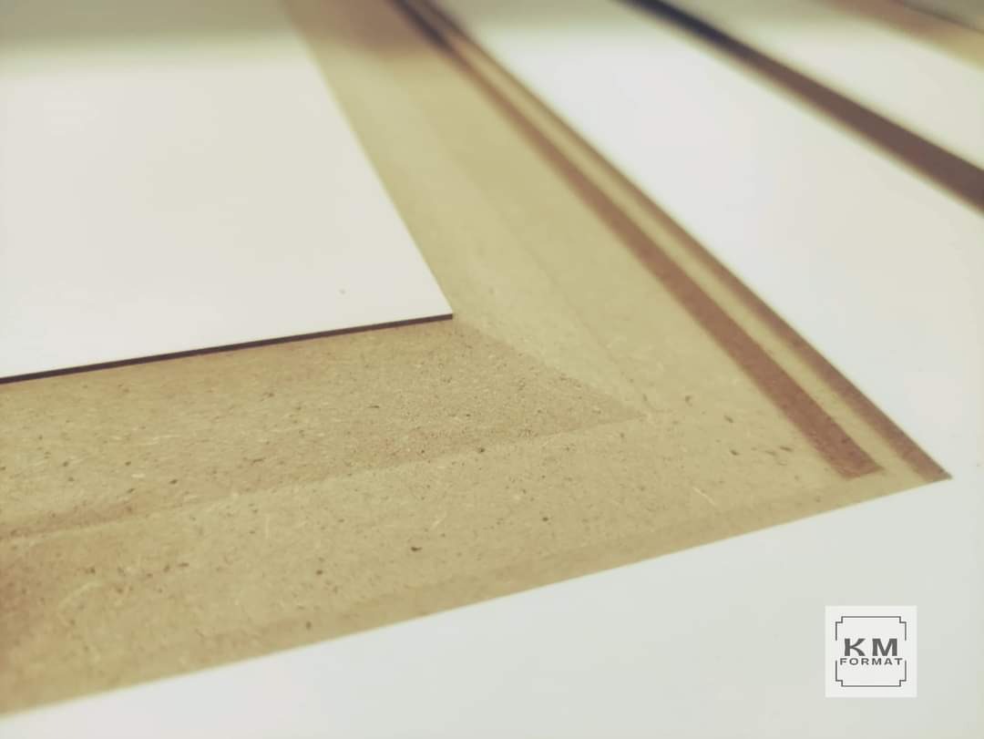 Fragment płyty MDF z wyfrezowanym obrysem pod białą płytę, widoczny logotyp 'KM FORMAT' w prawym dolnym rogu.