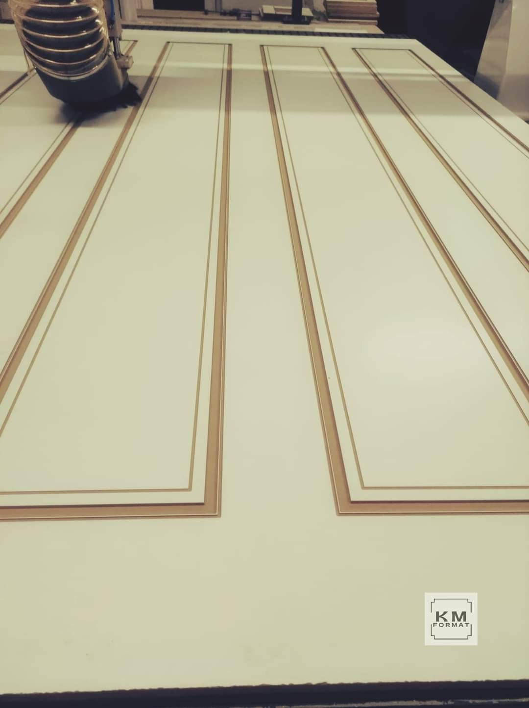 Frezarka CNC obrabia biały panel meblowy z dekoracyjnymi, brązowymi wstawkami. Widoczny fragment urządzenia i obrabiany element z bliska.