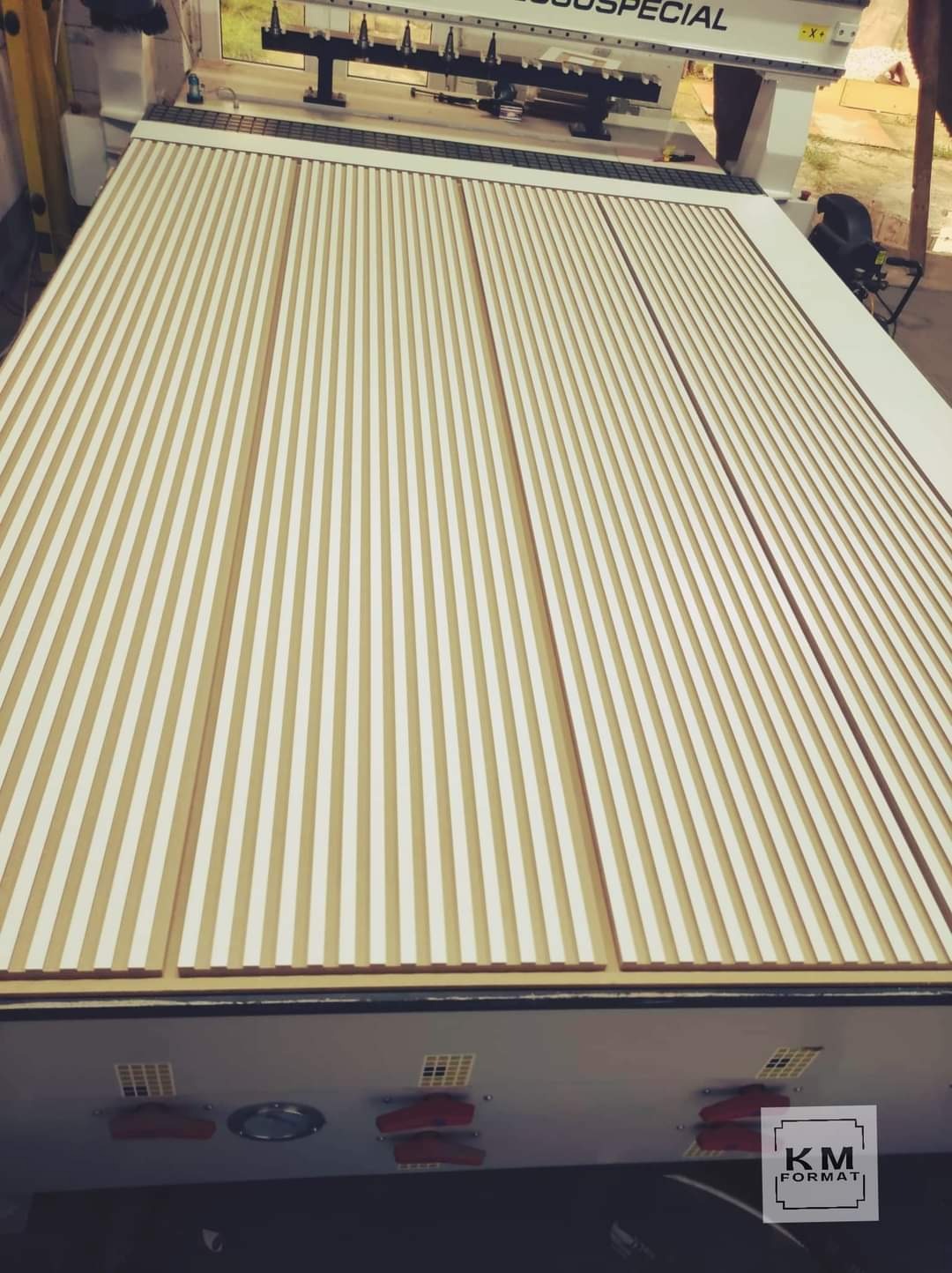 Frezowanie płyty MDF z pionowymi rowkami na ploterze CNC, widoczny blat roboczy maszyny i logo producenta.