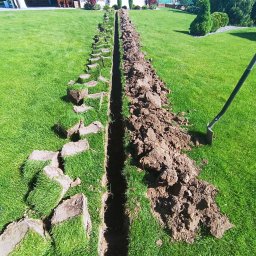 MyEnergy Sebastian Kurpiewski - Wykonany wykop w trawniku pod instalację, z wyciętymi fragmentami darni ułożonymi wzdłuż krawędzi, widoczny fragment szpadla wbitego w ziemię.