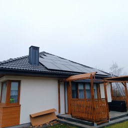 MyEnergy Sebastian Kurpiewski - Dom jednorodzinny z zainstalowanymi panelami słonecznymi na dachu, widoczne z poziomu ziemi w pochmurny dzień. Na pierwszym planie częściowo rozpakowane kartony.