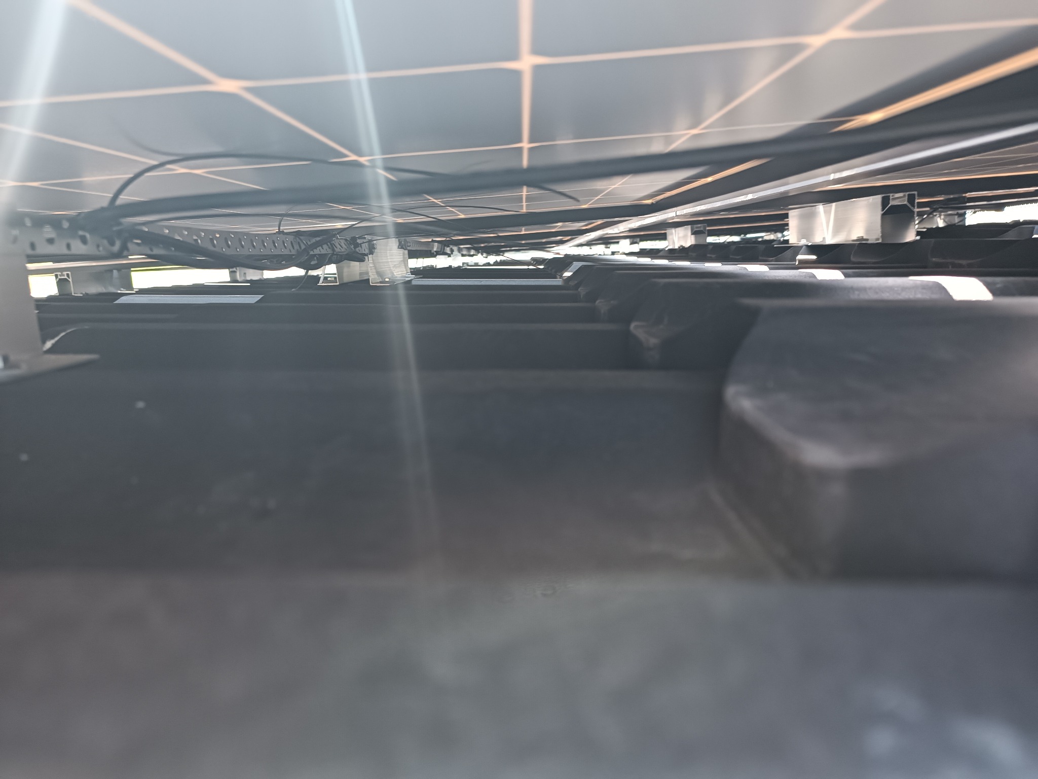 Widok od spodu na panele słoneczne zamontowane na dachu, widoczne kable i elementy konstrukcyjne mocowania.