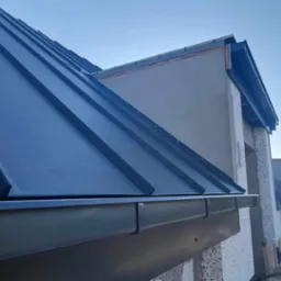 Nowe, grafitowe krycie dachu z blachy na budynku w trakcie budowy, widoczne rynny i rusztowania.