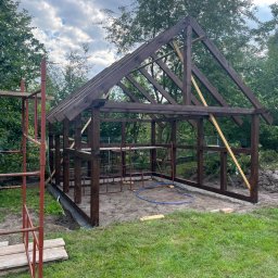 Usługi ogólnobudowlane Artur Zieliński - Konstrukcja drewniana altany w trakcie budowy, widoczne rusztowanie i elementy więźby dachowej na tle zieleni i pochmurnego nieba.