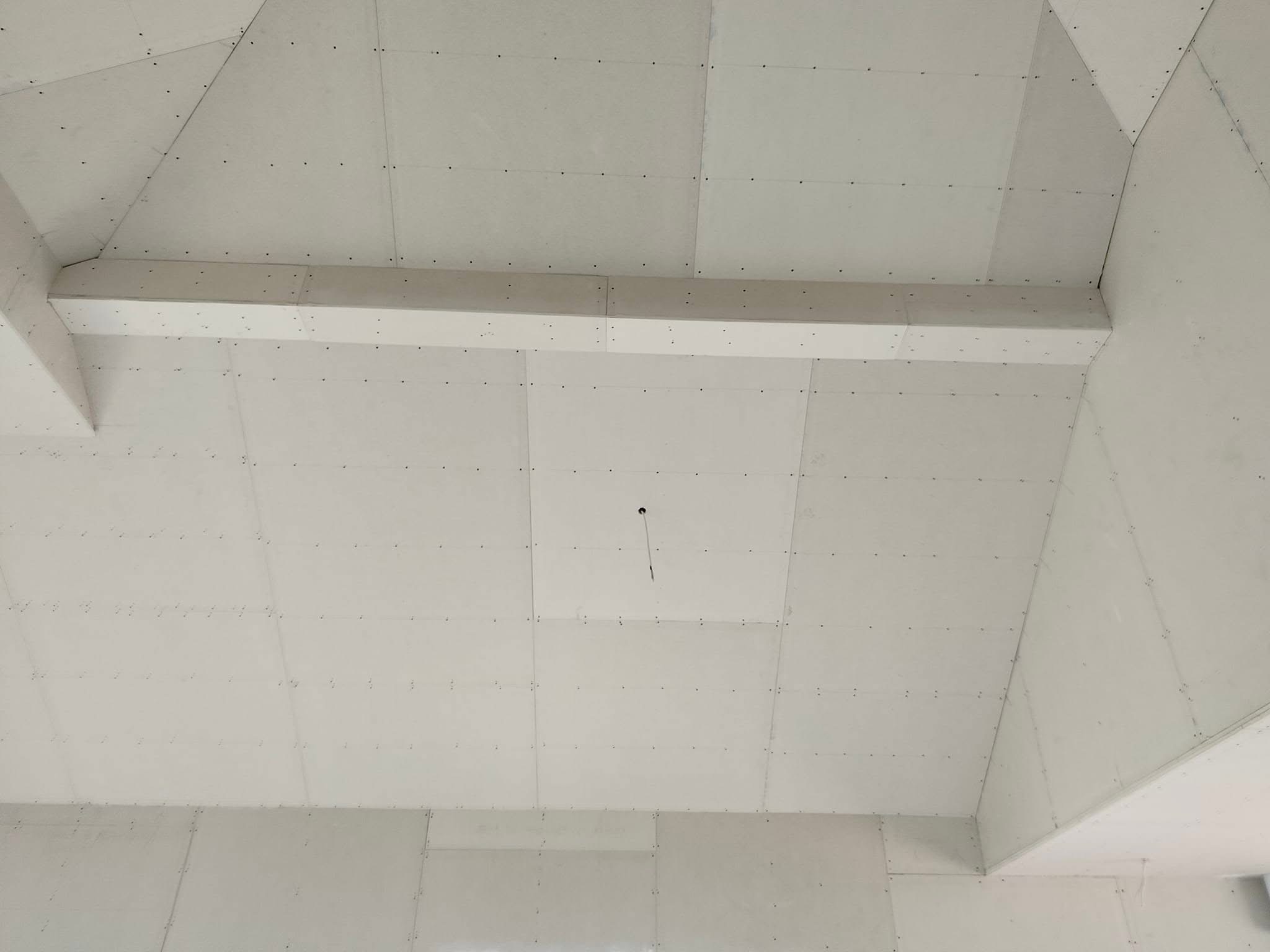 Sufit poddasza wykończony płytami gipsowo-kartonowymi, widoczne łączenia i wkręty, belka konstrukcyjna w poprzek sufitu, przewód elektryczny wystający z sufitu.