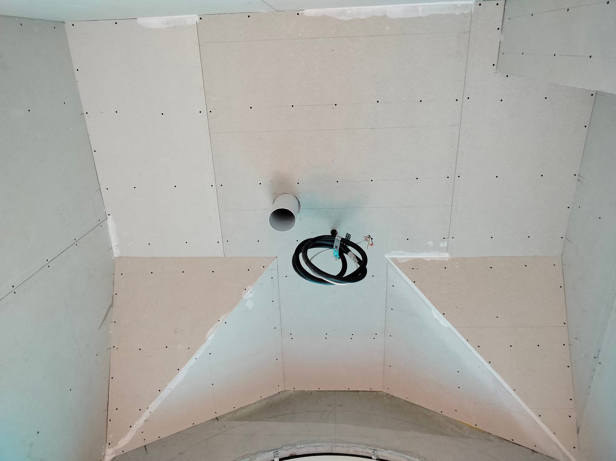 Sufit podwieszany w trakcie montażu, widoczne płyty gipsowo-kartonowe, łączenia szpachlowane, rura wentylacyjna i przewody elektryczne zwisające ze stropu.