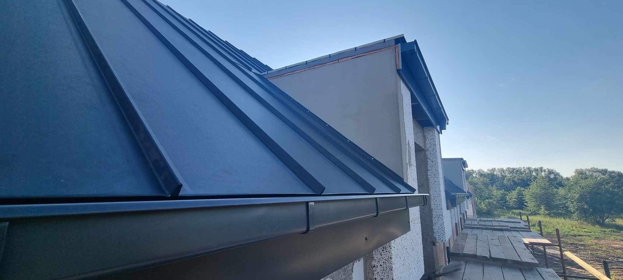 Nowe, grafitowe krycie dachu z blachy na budynku w trakcie budowy, widoczne rynny i rusztowania.