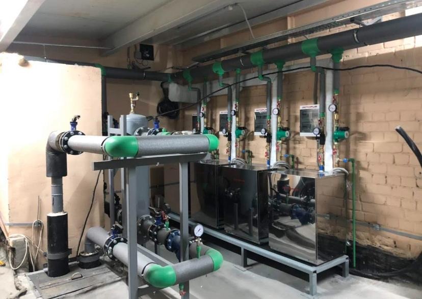 Kompleksowa instalacja grzewcza z rurami w izolacji, zaworami i pompami obiegowymi, zamontowana w piwnicy z ceglanymi ścianami.