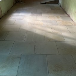 KOLART-BRUK Mykola Chermenskyi - Jasne, prostokątne płyty kamienne ułożone w korytarzu. Widoczne narzędzia i oświetlenie budowlane. Realizacja w Gryfowie Śląskim.