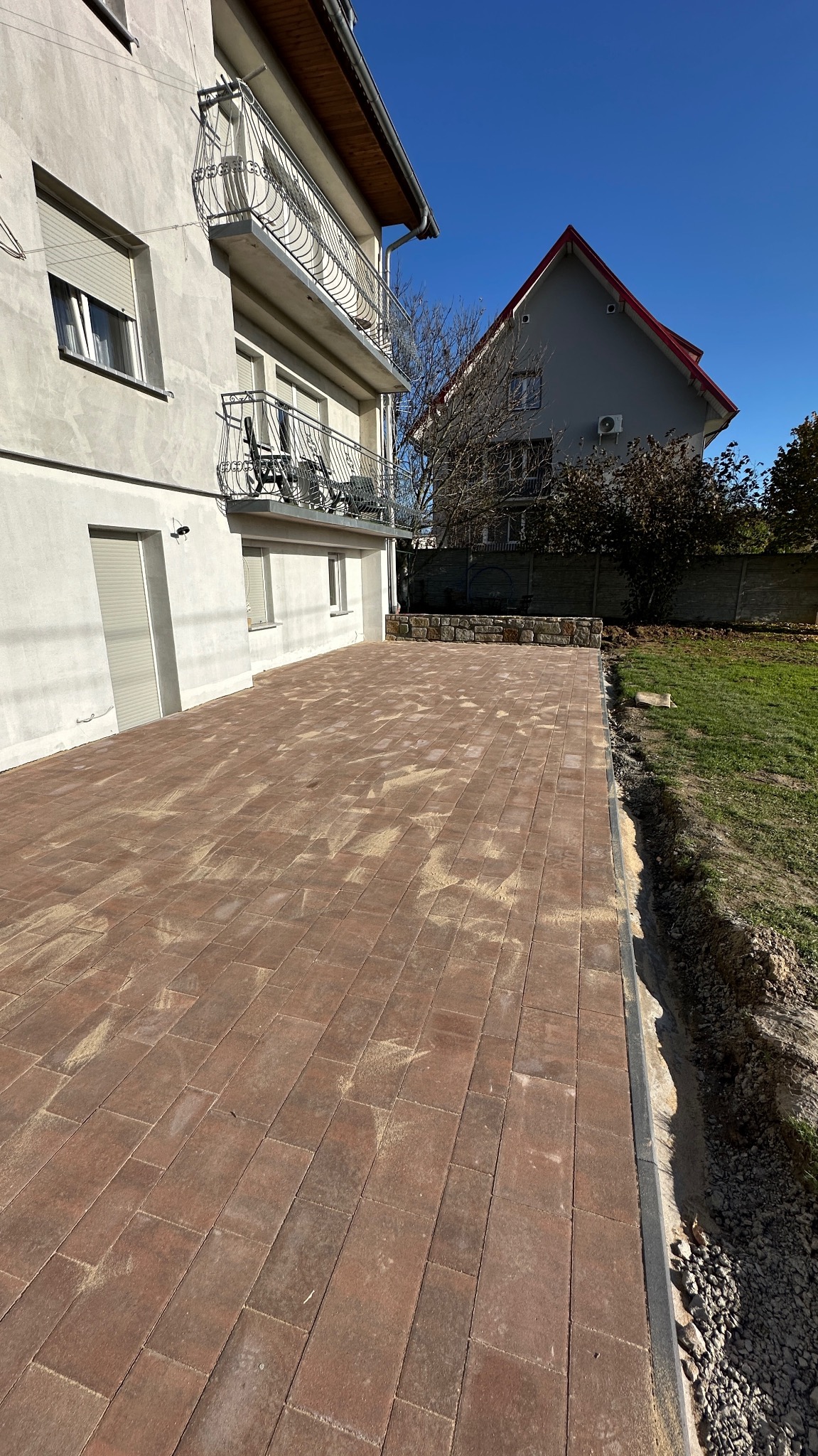 Nowo ułożona, brązowa kostka brukowa przed domem z balkonem, w słoneczny dzień. Widoczne detale wykończenia i przygotowane podłoże.