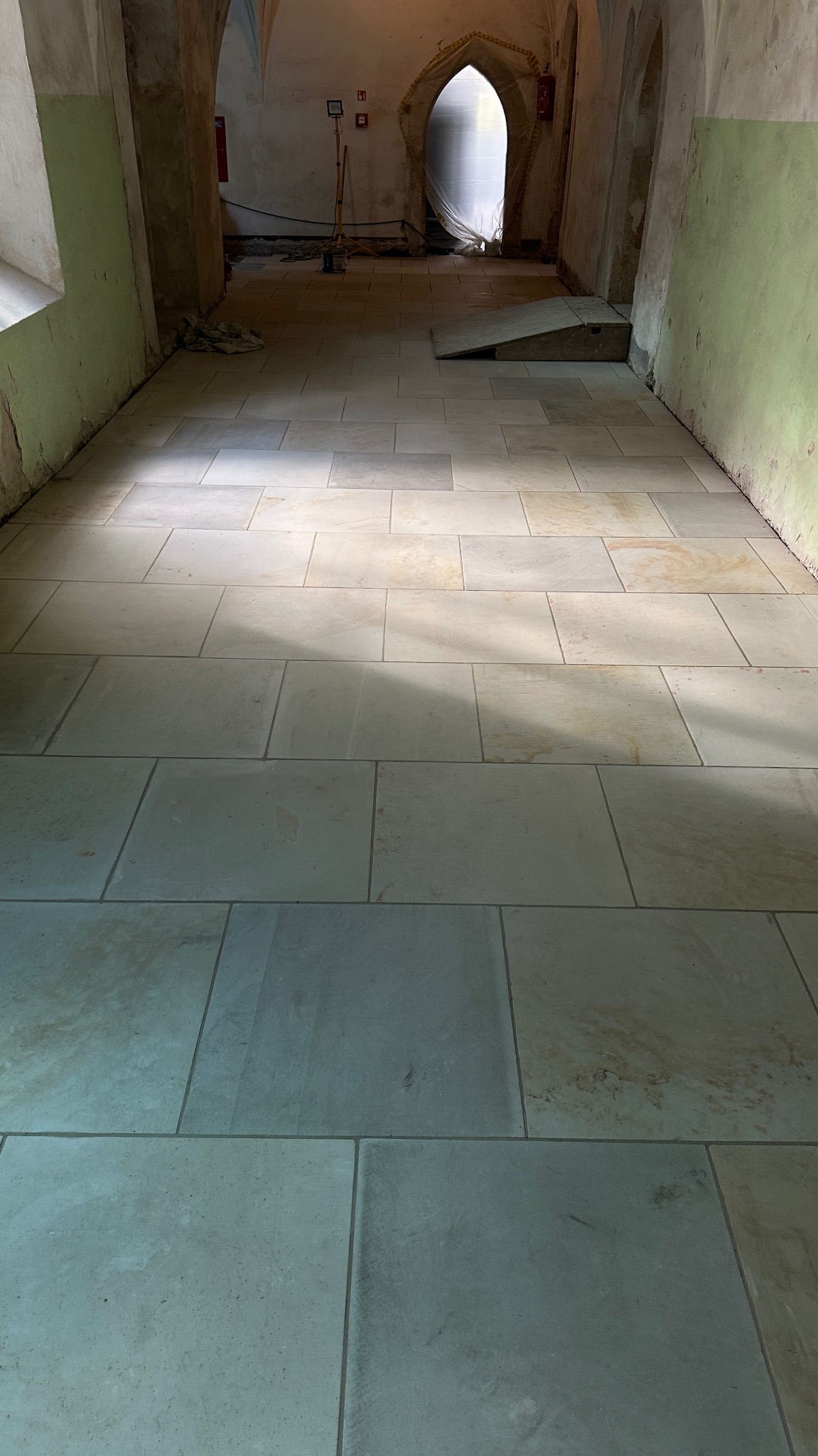 Jasne, prostokątne płyty kamienne ułożone w korytarzu. Widoczne narzędzia i oświetlenie budowlane. Realizacja w Gryfowie Śląskim.