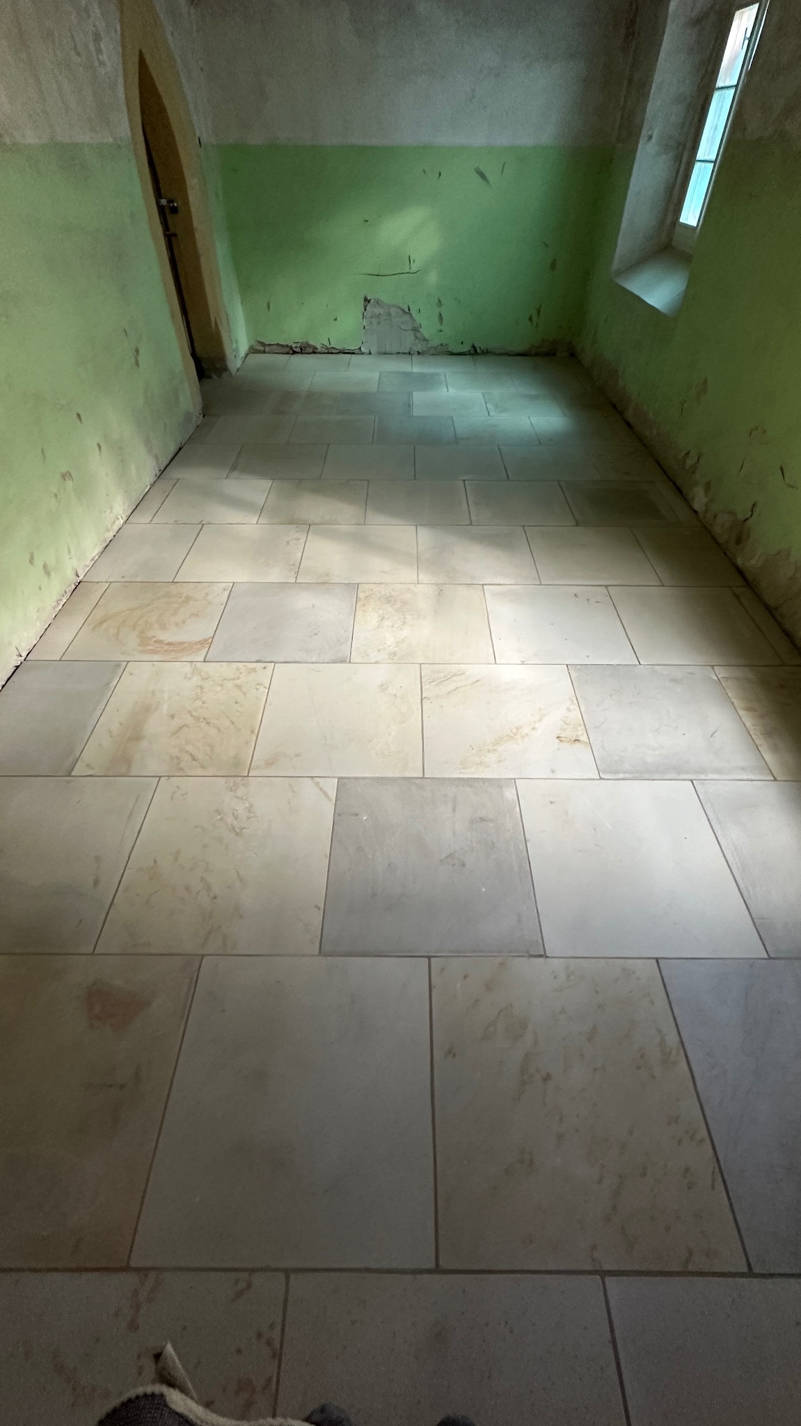 Ułożona podłoga z kamiennych płyt w pomieszczeniu z zielonymi ścianami i oknem. Widoczne nieregularne kształty pomieszczenia i naturalne światło.