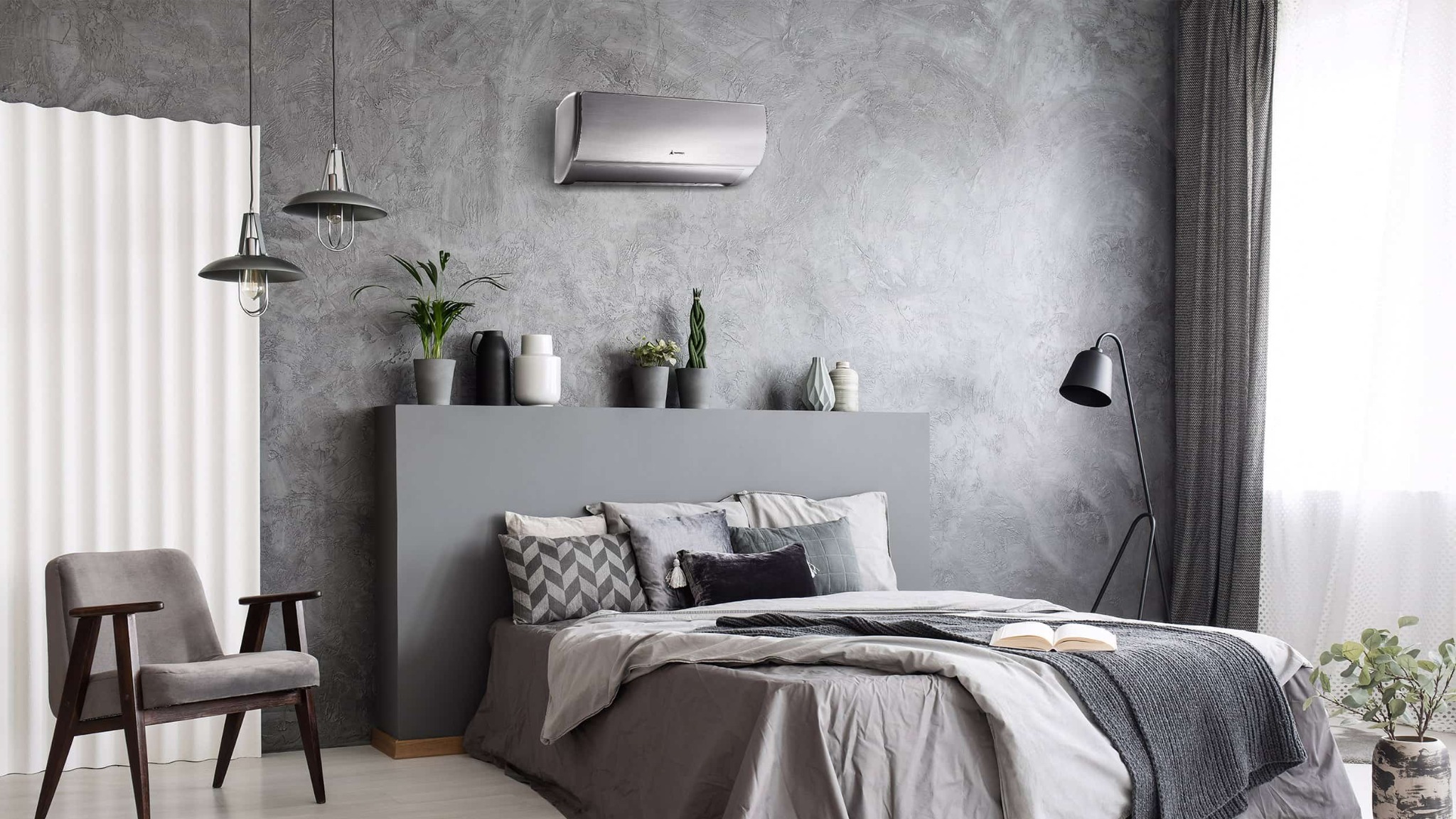 Nowoczesny klimatyzator srebrny zamontowany na szarej ścianie w sypialni z łóżkiem, lampami i dekoracjami.
