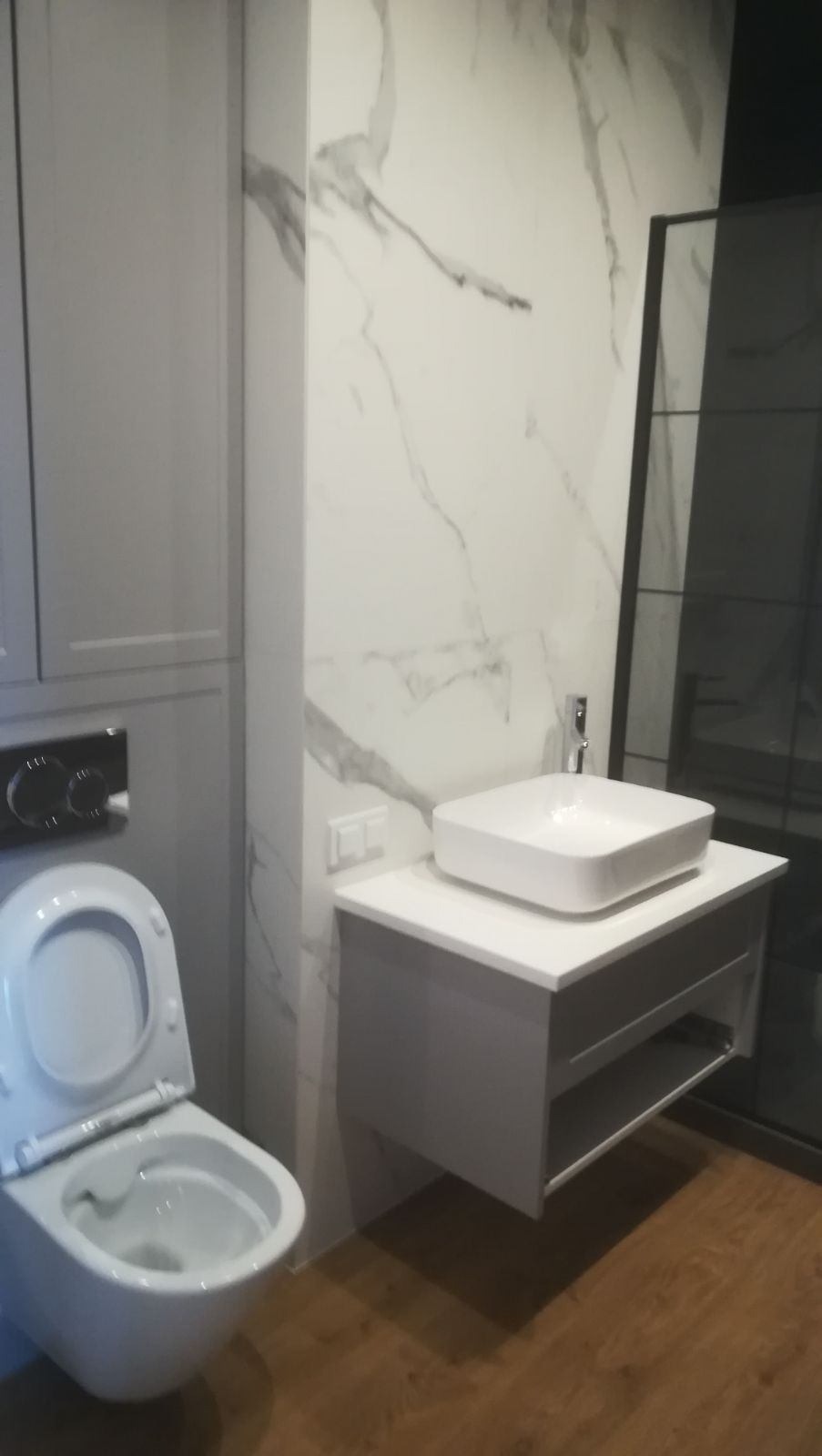Nowoczesna łazienka z podwieszaną toaletą, umywalką nablatową i płytkami imitującymi marmur na ścianie.