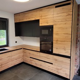 Gggg - Nowoczesna kuchnia z drewnianymi frontami i czarnymi akcentami, w tle ceglana ściana i widok na zewnątrz przez okno.