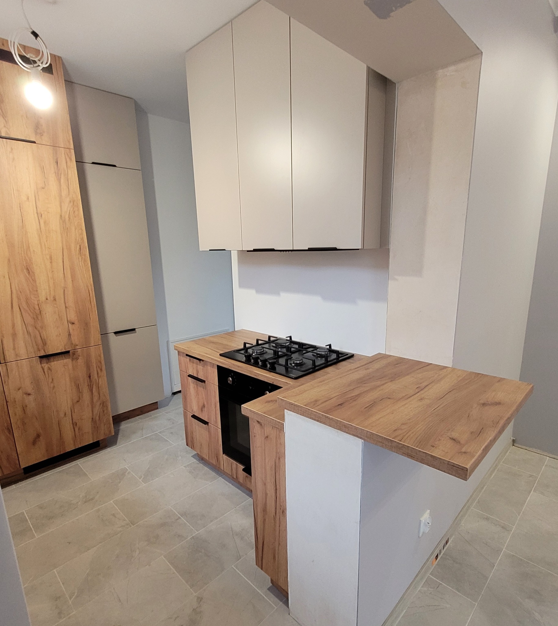 Nowoczesna kuchnia z drewnianymi frontami szafek i blatem w odcieniach brązu, uzupełniona białymi szafkami wiszącymi i półwyspem z blatem.