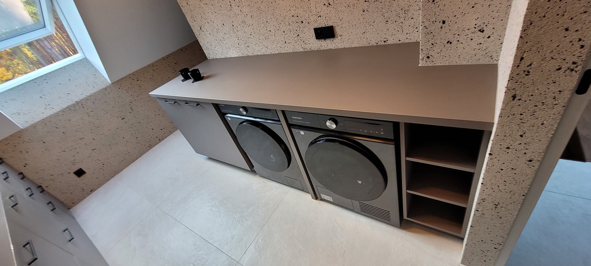 Nowoczesna pralnia z zabudową meblową w odcieniach szarości, z pralką i suszarką Samsung pod blatem, widok z góry.