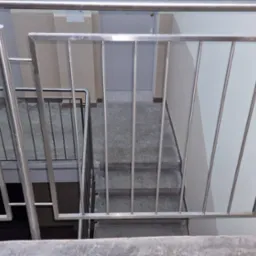 Wewnętrzne schody z poręczami ze stali nierdzewnej, widok z góry na kilka stopni, z fragmentem otwartej książki w lewym górnym rogu.