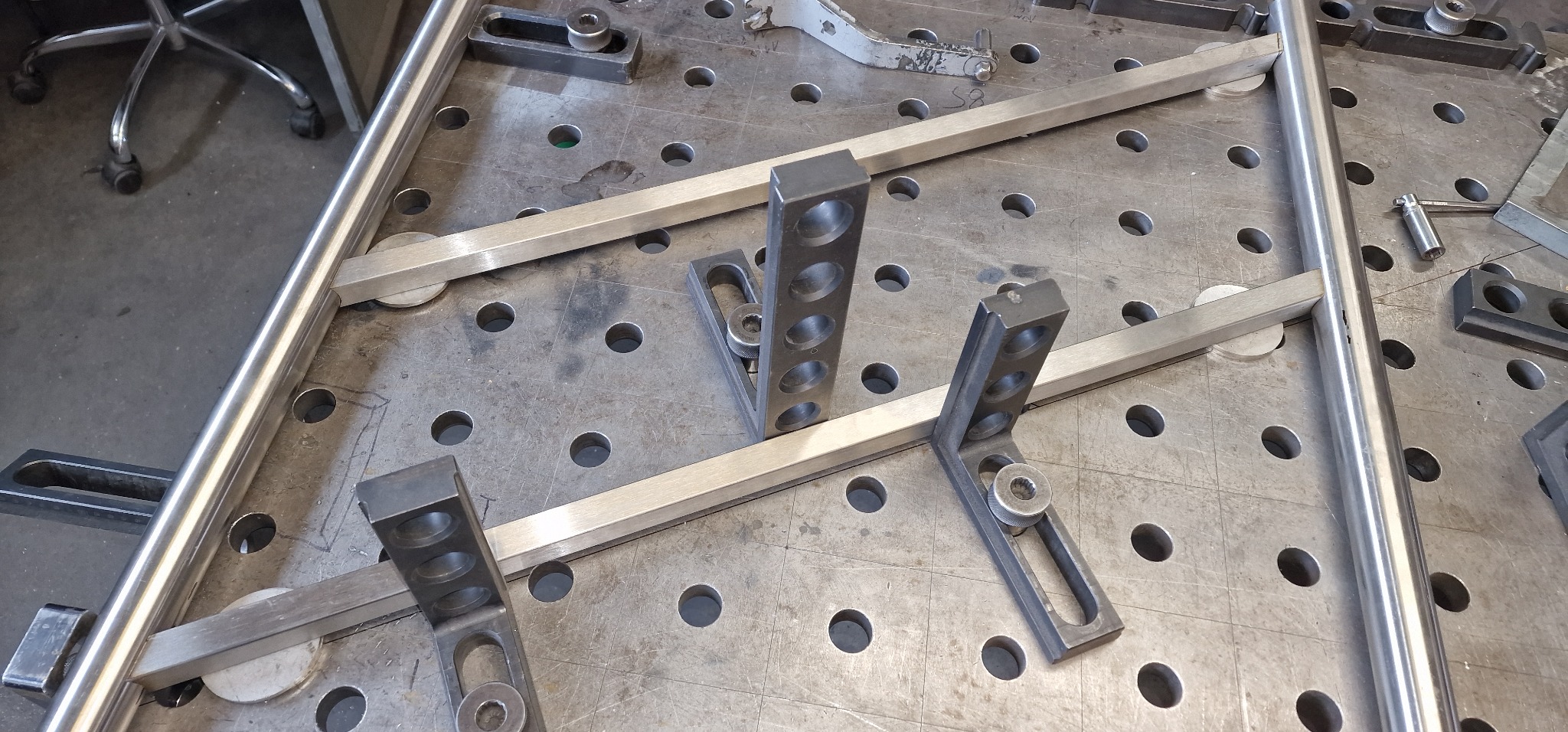 Elementy metalowe, rury i kątowniki z otworami, ułożone na perforowanym stole spawalniczym, przygotowane do spawania