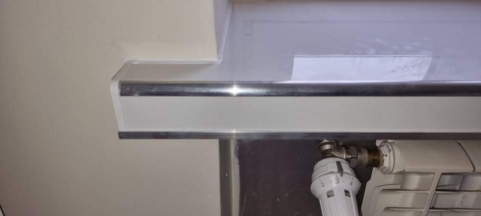 Szczegół wykończenia ściany przy grzejniku z termostatem, widoczne listwy przypodłogowe i rura grzewcza.