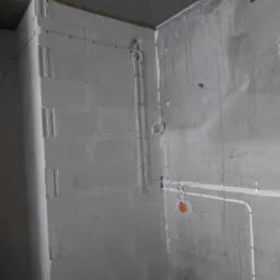 Surowe wnętrze w trakcie prac: widoczne przewody elektryczne zamocowane na ścianie z betonu komórkowego oraz na surowej ścianie betonowej z odręcznymi notatkami, pomarańczowe puszki instalacyjne.