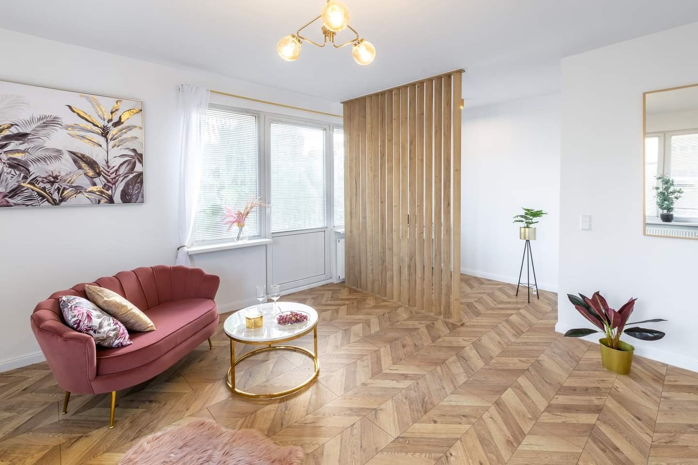 Jasne, przestronne wnętrze z parkietem w jodełkę, różową sofą, marmurowym stolikiem kawowym i drewnianą ażurową ścianką działową.