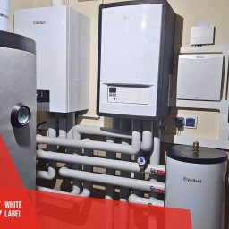 White Label Sp. z o.o. - Instalacja kotłów grzewczych Vaillant z widocznymi rurami i zbiornikami, manometr na rurze, zamontowane w pomieszczeniu z jasnymi ścianami.