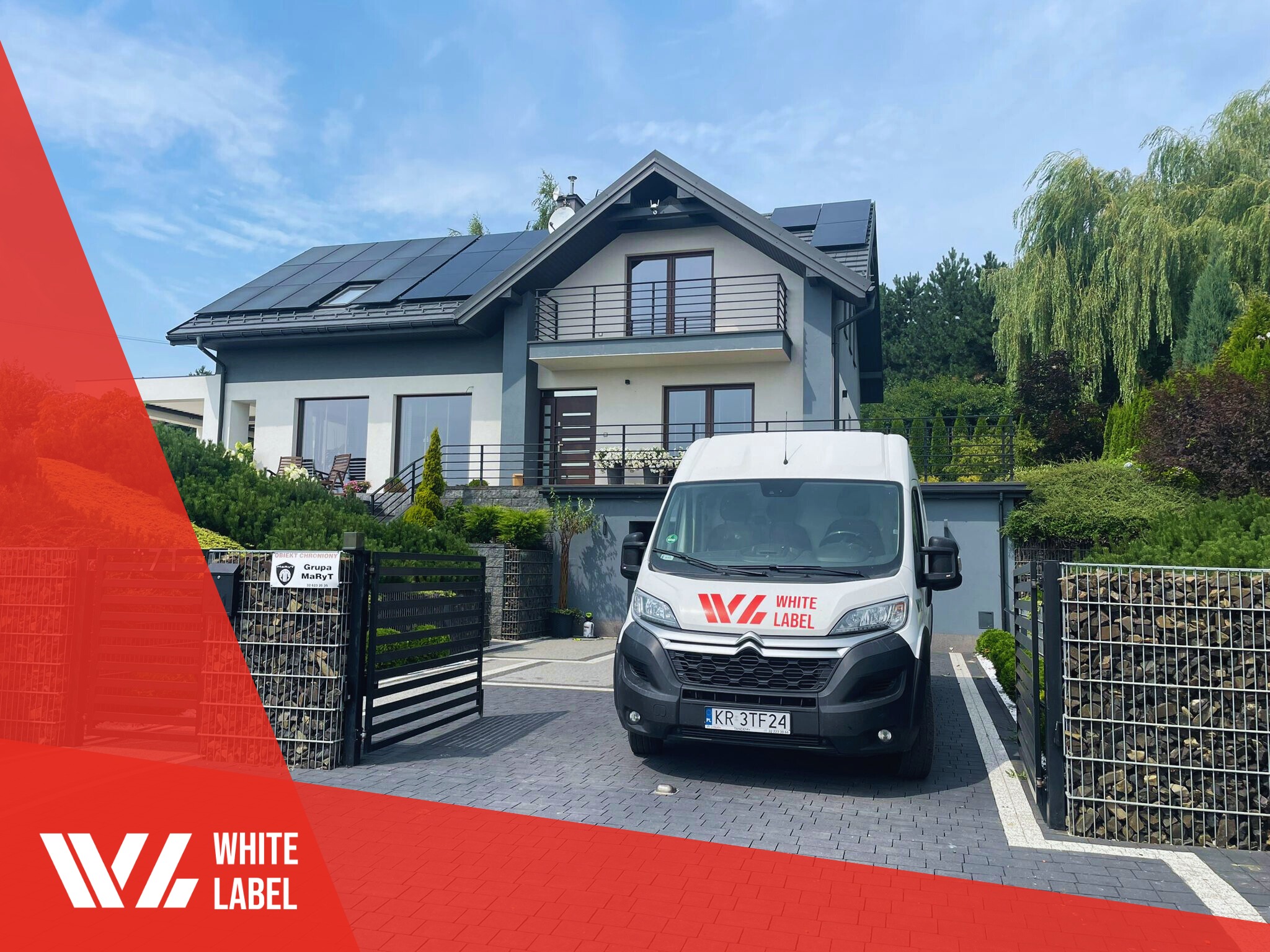 Nowoczesny dom jednorodzinny z panelami słonecznymi na dachu, biały bus firmy instalacyjnej White Label zaparkowany na podjeździe z kostki brukowej, brama wjazdowa z gabionami.