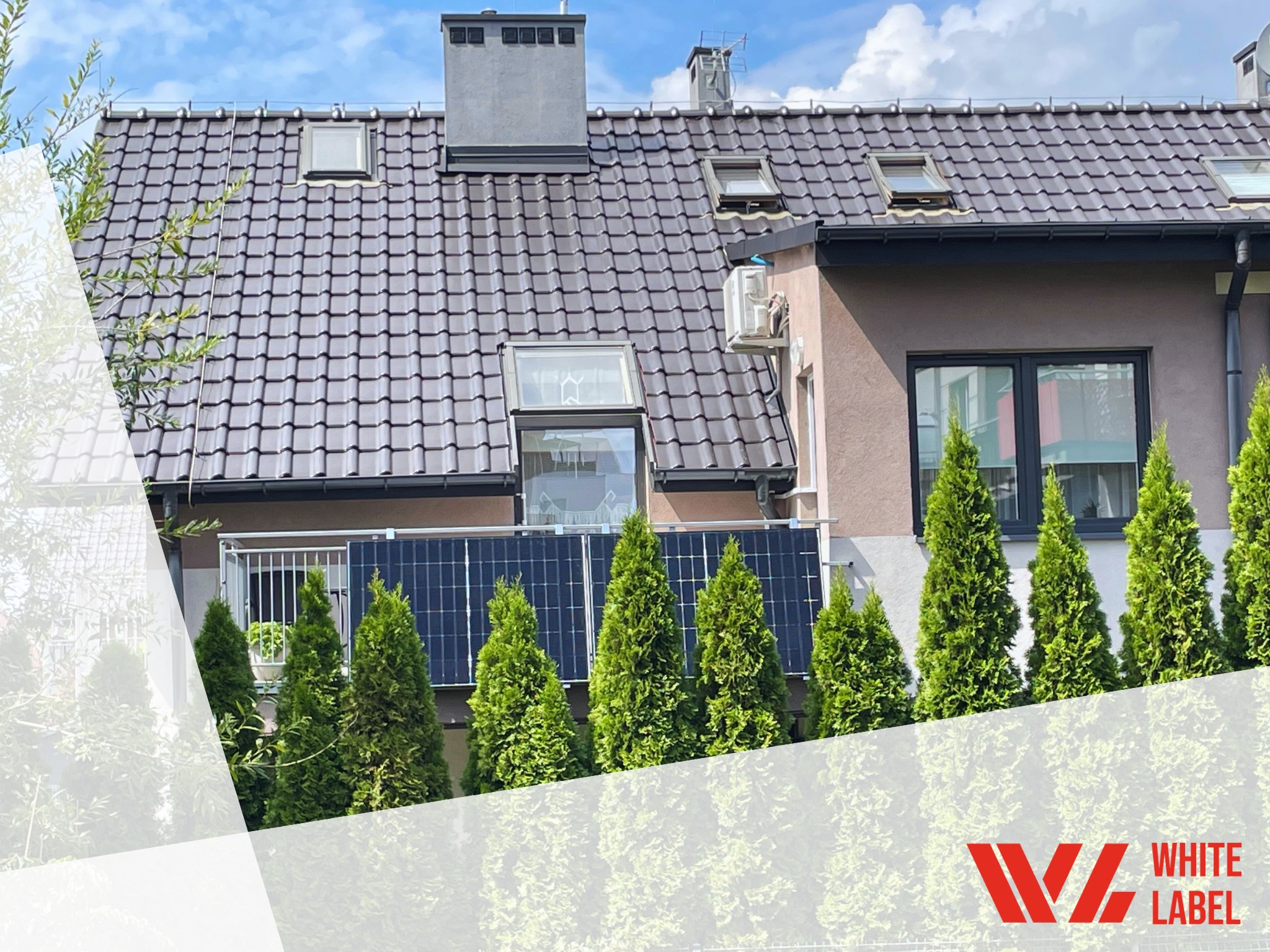 Panele słoneczne zamontowane na balkonie domu jednorodzinnego, widoczne zza rzędu wysokich tuj, z klimatyzatorem na ścianie i brązową dachówką.