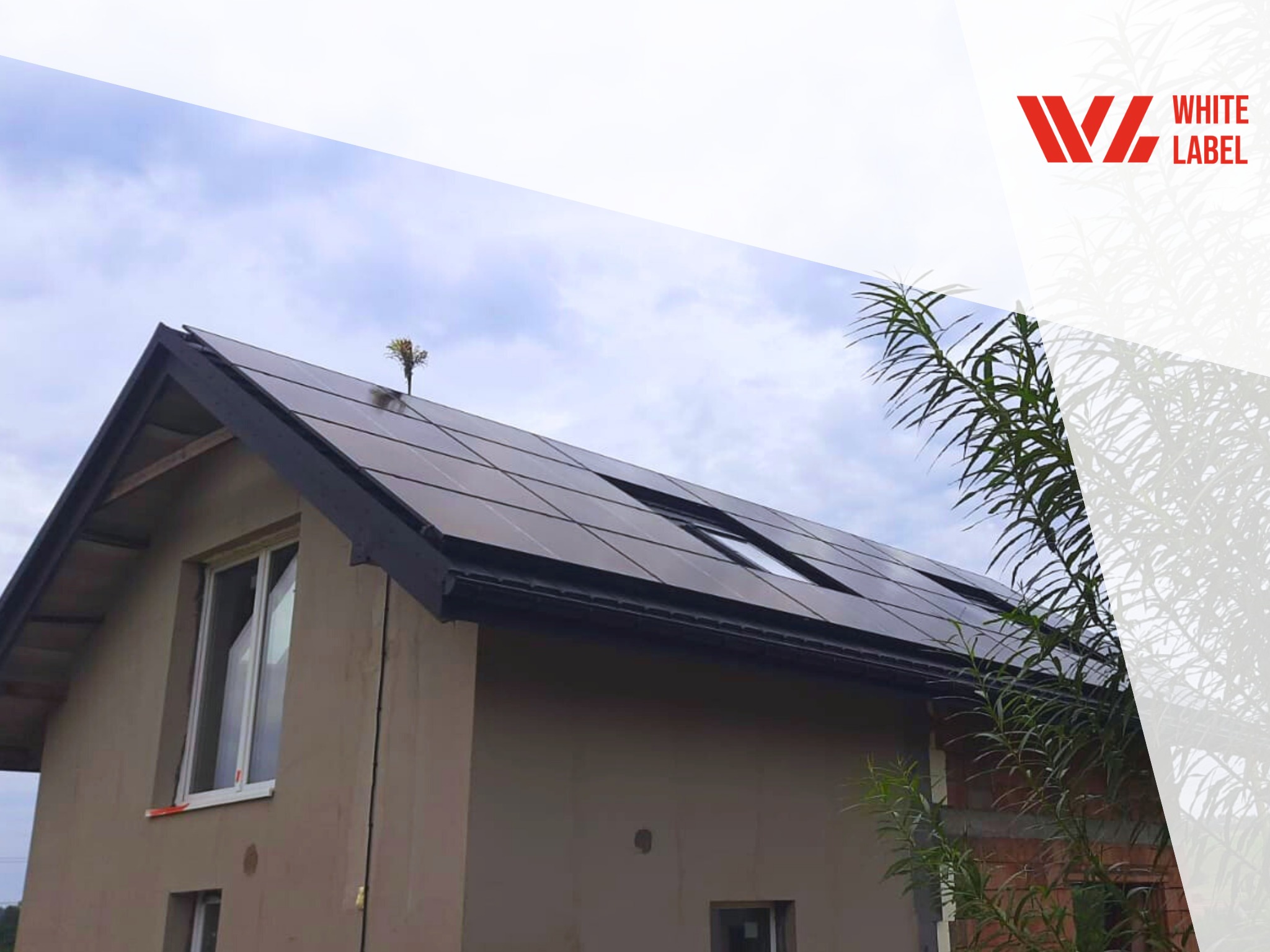 Częściowy widok domu jednorodzinnego z zamontowanymi czarnymi panelami słonecznymi na dachu, widoczne okno dachowe i elewacja w trakcie wykończenia, nałożone logo firmy w prawym górnym rogu.