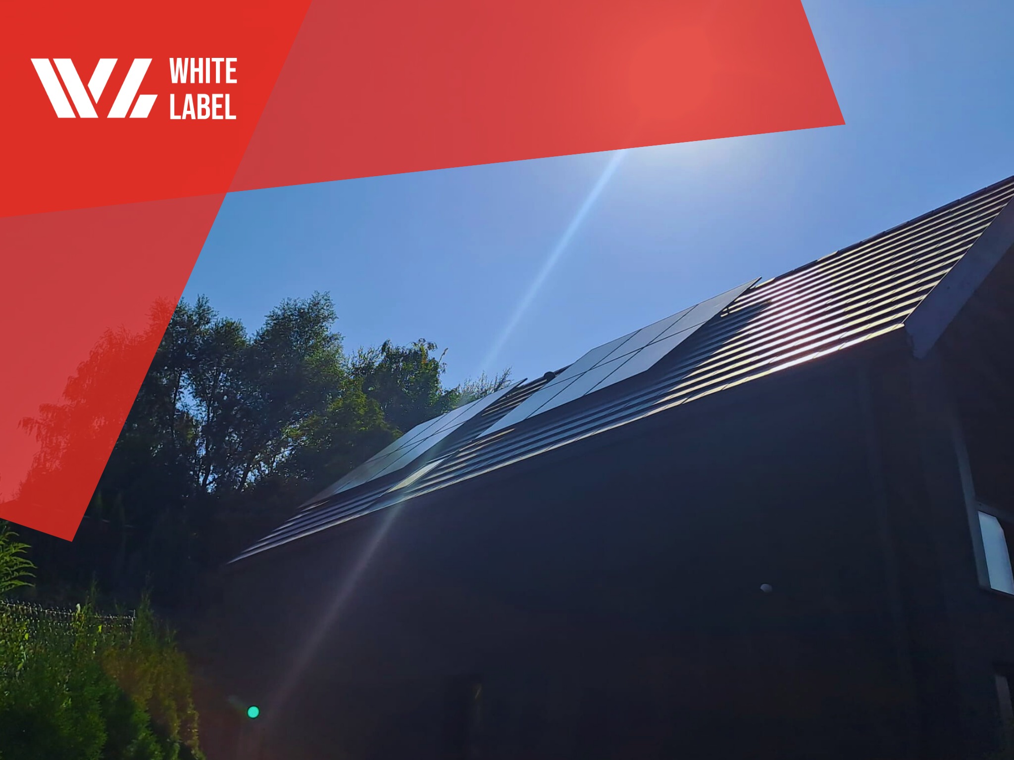 Czarny budynek z panelami słonecznymi na dachu, widok z dołu, logo firmy w lewym górnym rogu, błękitne niebo.