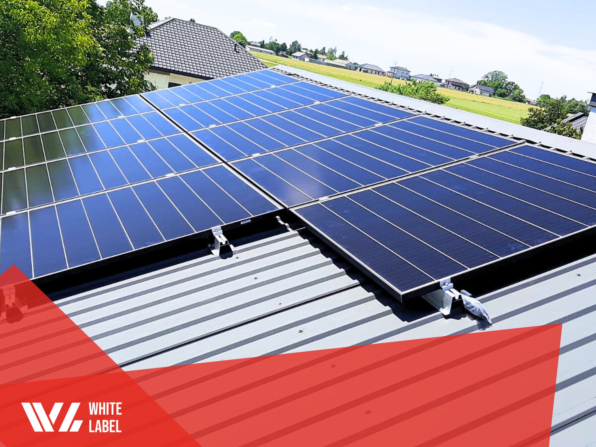 Panele słoneczne na dachu z blachy trapezowej, widok z dołu, w tle domy i drzewa, w rogu logo firmy.