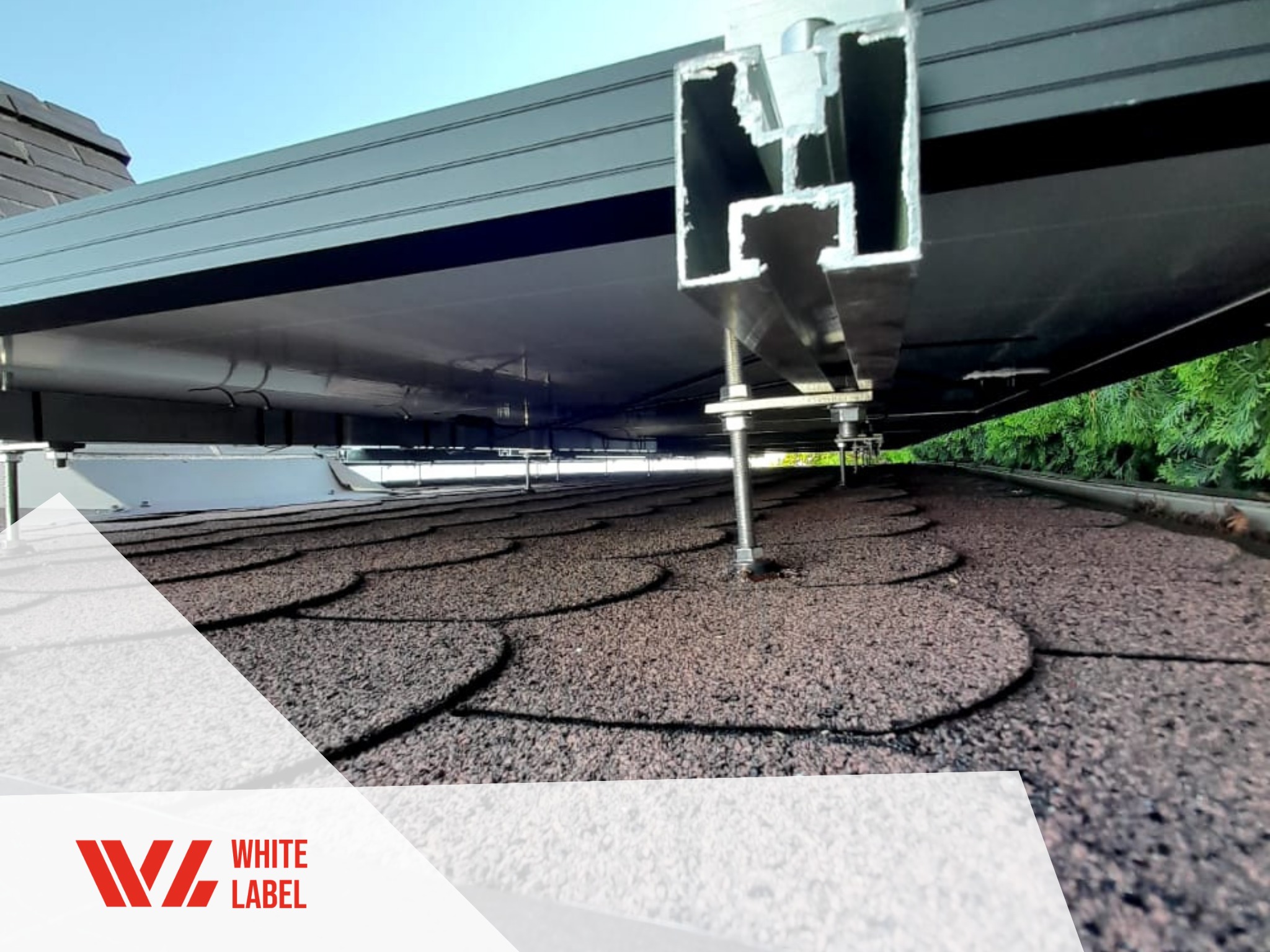 Montaż konstrukcji wsporczej pod panele na dachu pokrytym gontem bitumicznym, widoczne aluminiowe profile montażowe i śruby regulacyjne, w tle zieleń.