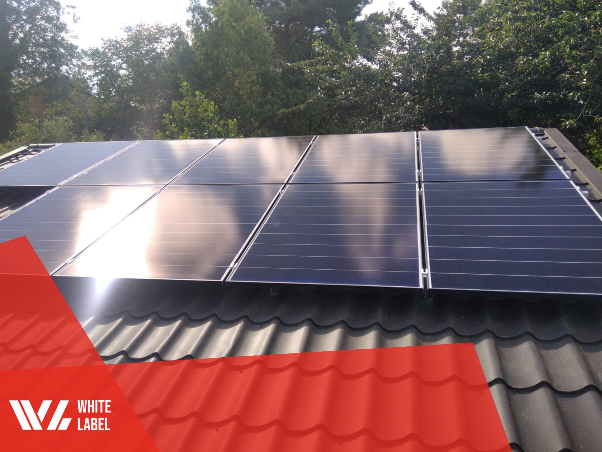 Panele słoneczne na dachu z ciemnej blachy falistej, częściowo zasłonięte czerwonym elementem graficznym z logo firmy.