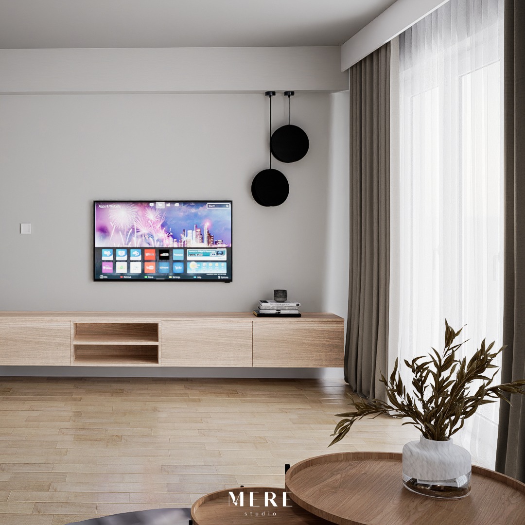 Jasne wnętrze salonu z drewnianą podłogą i szafką RTV, na ścianie telewizor i okrągłe lampy, minimalistyczny wystrój z zasłonami i stolikiem kawowym z rośliną w wazonie.