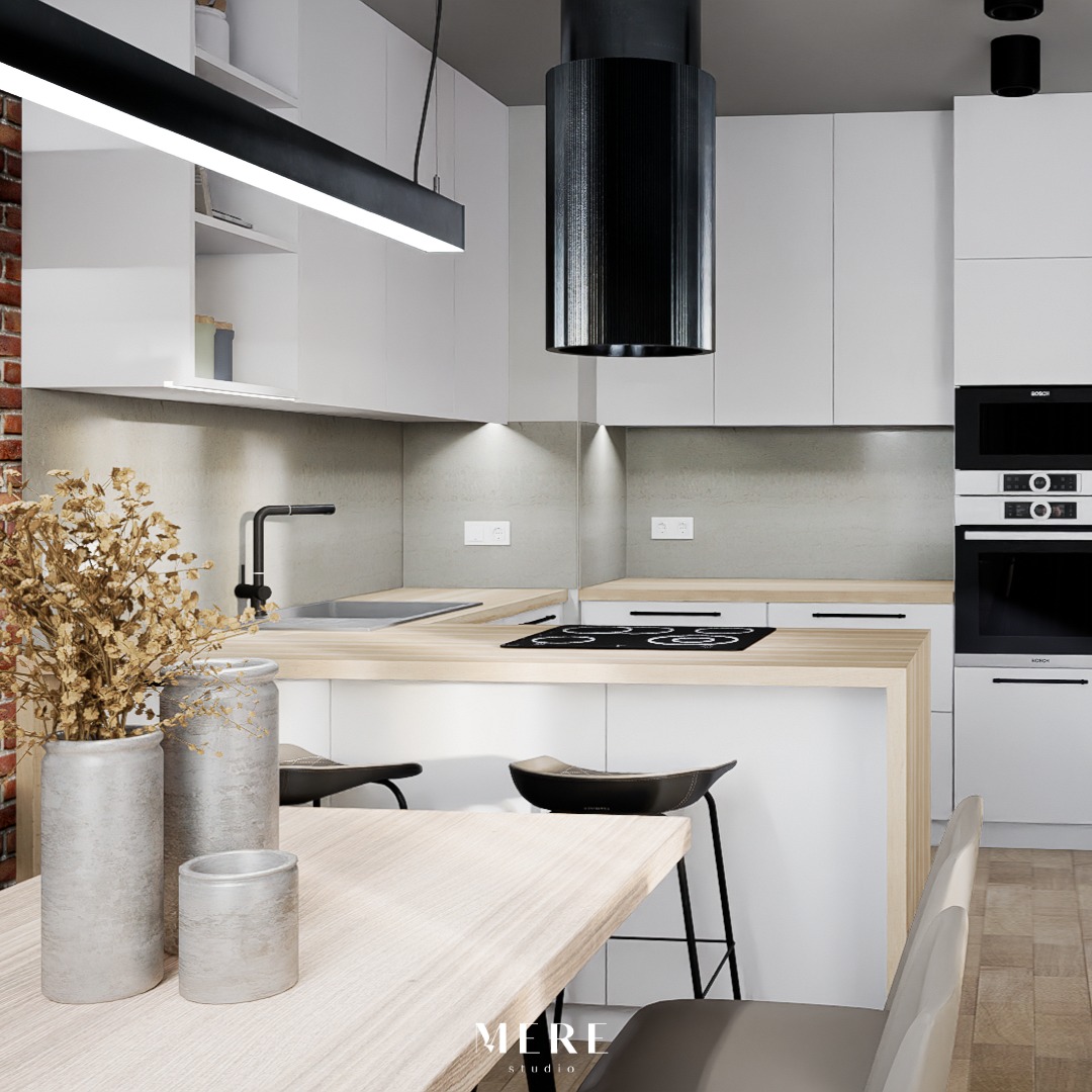 Nowoczesna, minimalistyczna kuchnia z białymi szafkami, drewnianym blatem, czarnym okapem cylindrycznym i ceglaną ścianą w tle. Na pierwszym planie drewniany stół z dekoracyjnymi wazonami.