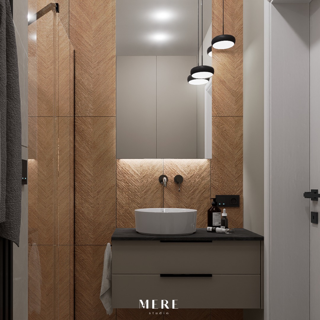 Nowoczesna łazienka z umywalką nablatową, drewnianą mozaiką na ścianach, minimalistyczną szafką pod umywalką w odcieniach szarości i czarnymi lampami wiszącymi.